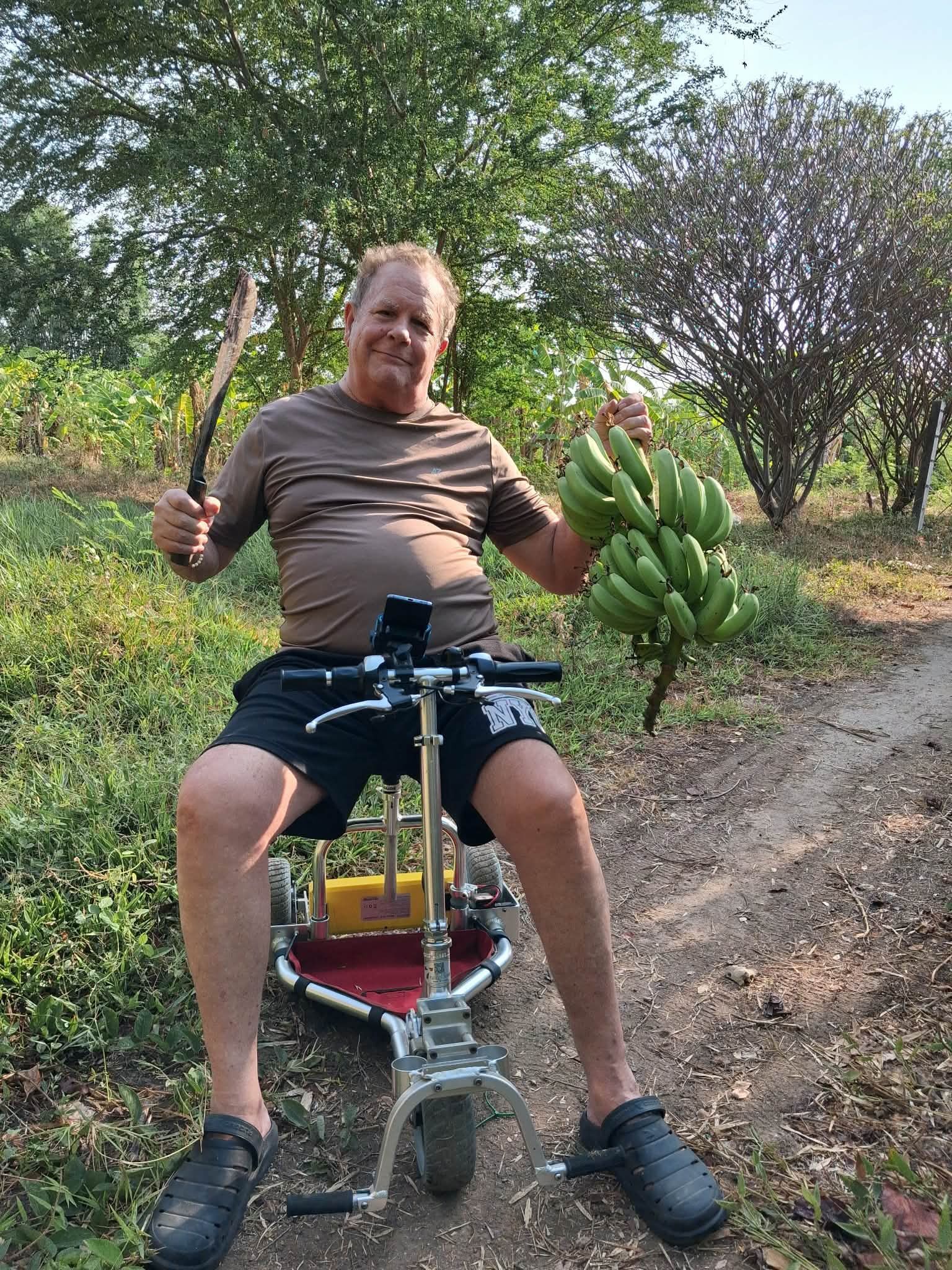 A man holding a machete and a bunch of bananas on a mobility scooter.