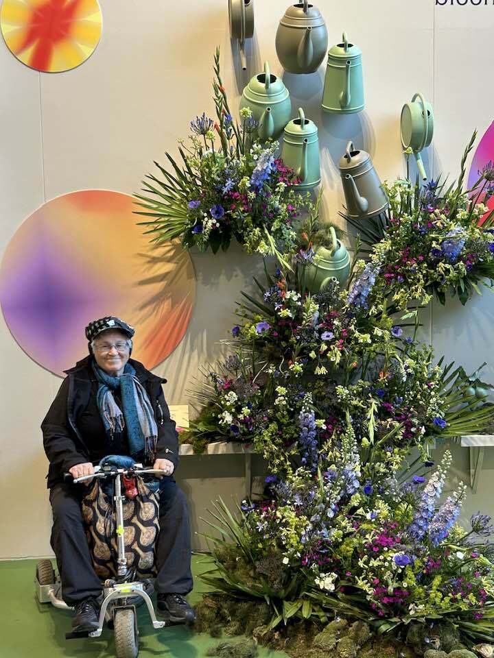 Woman on mobility scooter in front of a large assortment of flowers.