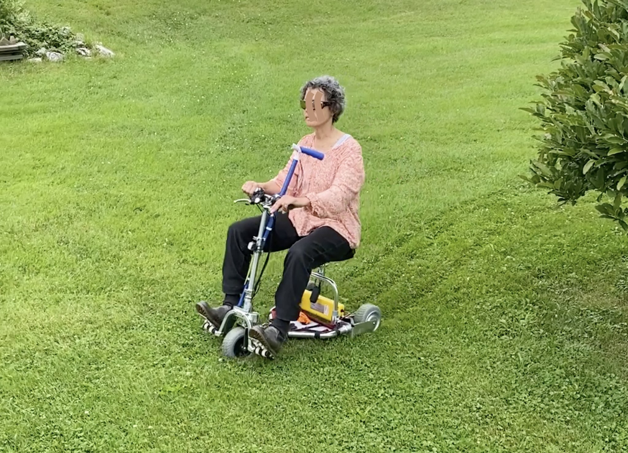 Man riding down a grassy hill on a mobility scooter.